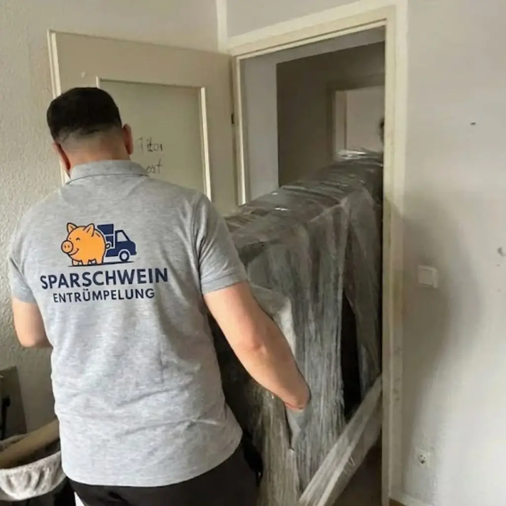 Mitarbeiter trägt verpackte Möbel durch enge Tür bei einer Dachbodenräumung